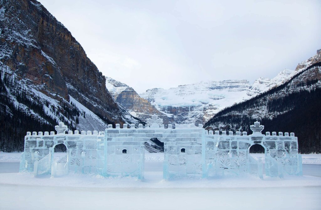 An ice sculpture of a castle sat in the snow in front of a mountainous backdrop.